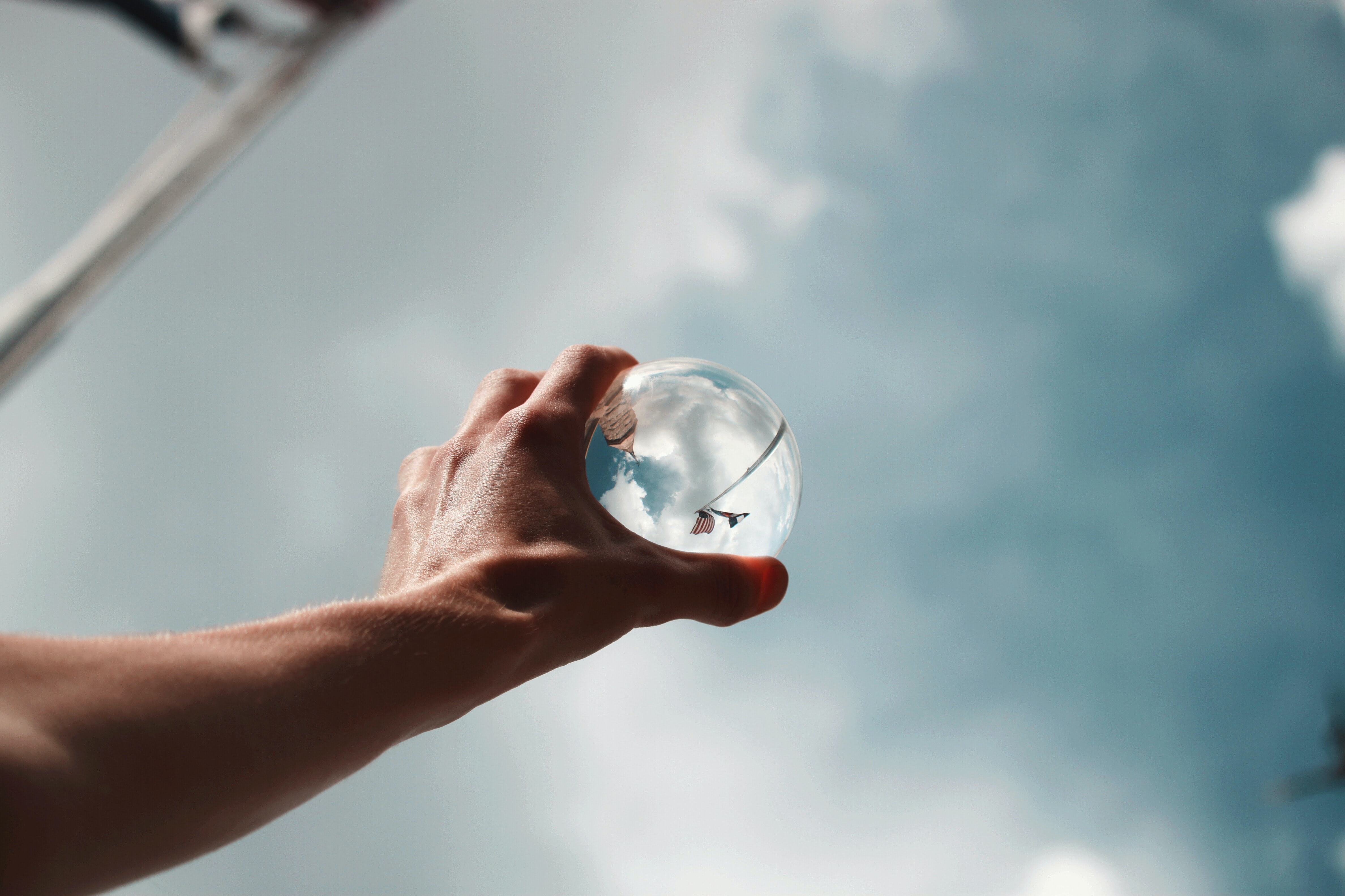 a hand holding a glass sphere to the sky with inverted reflections of a flag and building